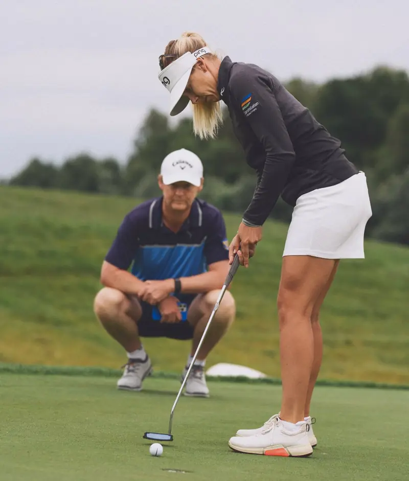 A player putting while her caddie reads the line